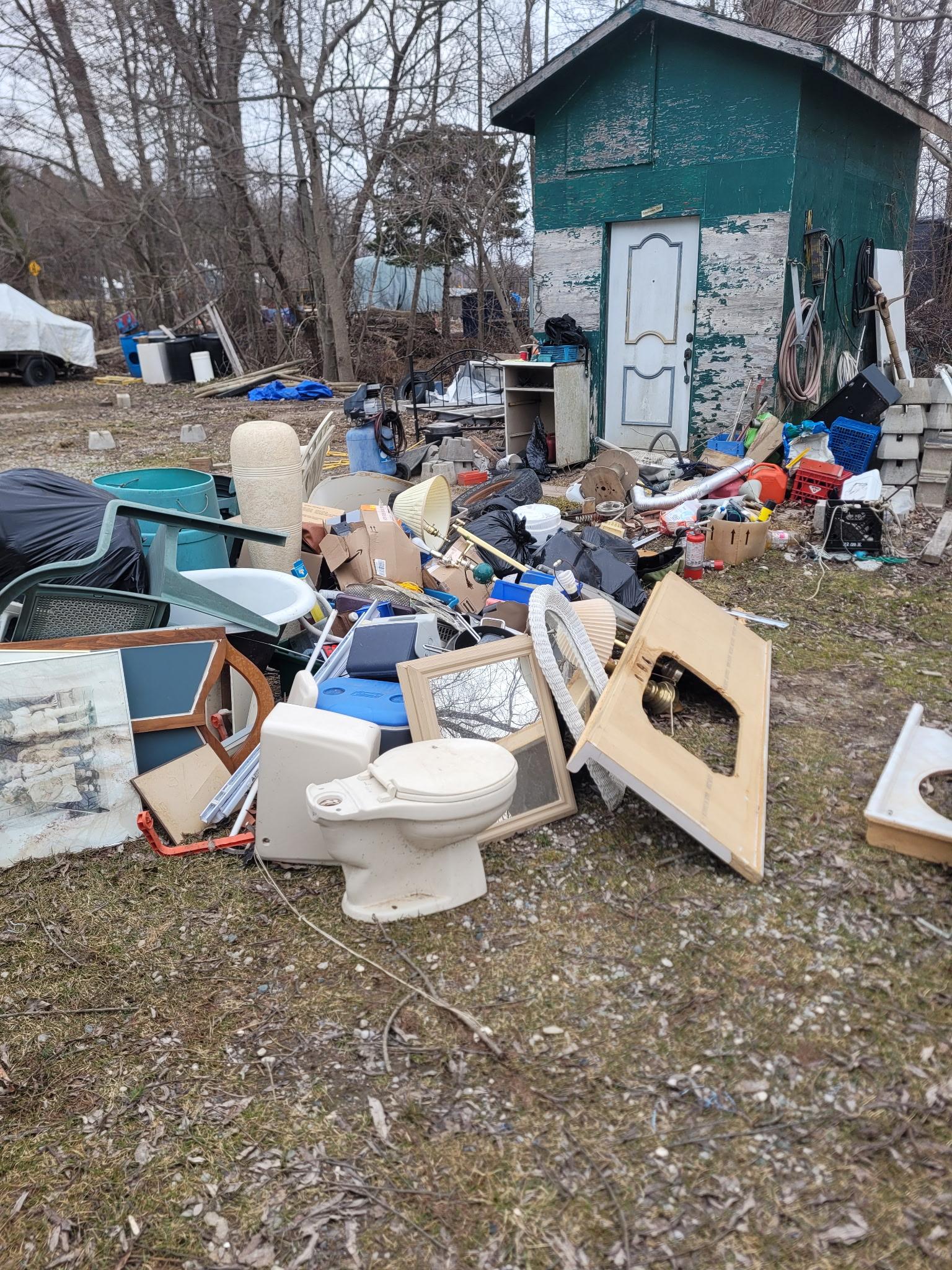 Cluttered yard before junk removal — St. Thomas, Ontario. Toilet, wood, old furniture piled up.